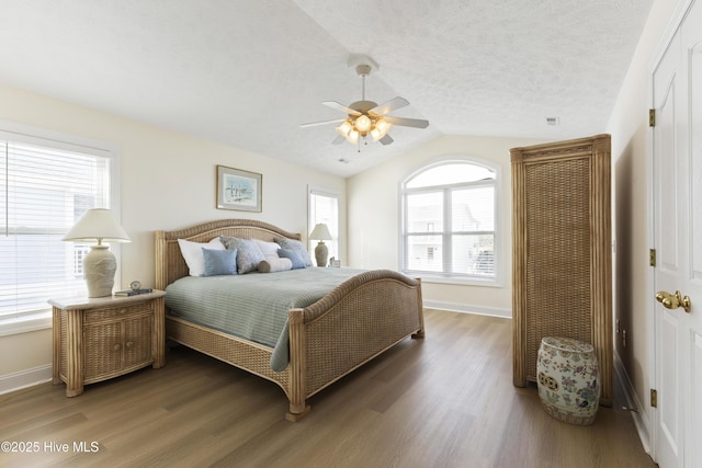 bedroom with a textured ceiling, baseboards, vaulted ceiling, and wood finished floors