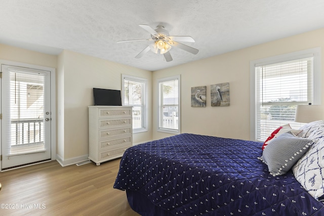 bedroom with access to exterior, multiple windows, a textured ceiling, and wood finished floors