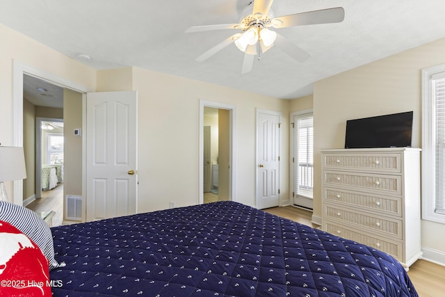 bedroom with connected bathroom, wood finished floors, a ceiling fan, visible vents, and baseboards