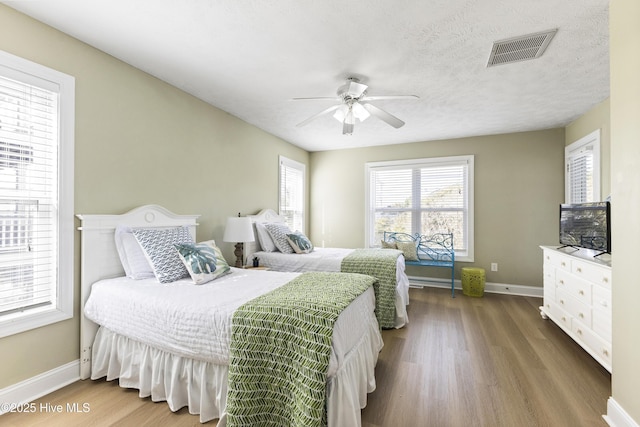 bedroom with baseboards, a textured ceiling, visible vents, and wood finished floors