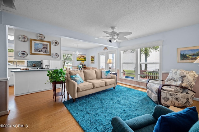 living area with light wood-style floors, a textured ceiling, and ceiling fan with notable chandelier