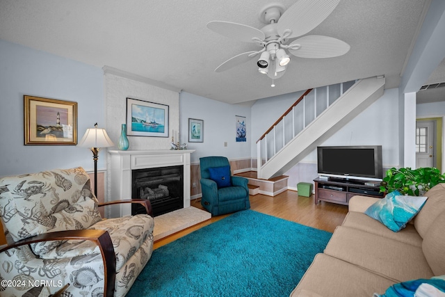 living area featuring visible vents, stairway, a ceiling fan, a glass covered fireplace, and wood finished floors