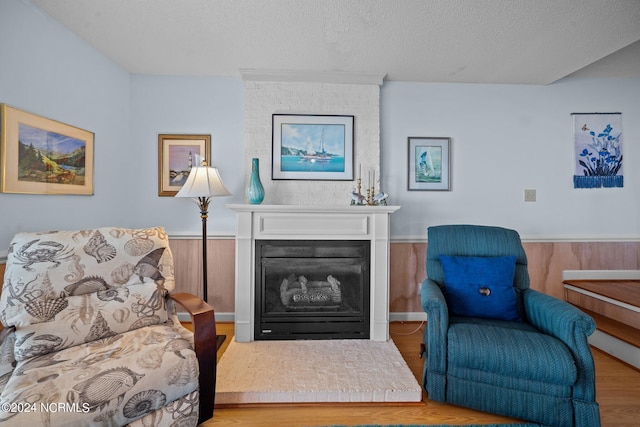 living area with a glass covered fireplace, a wainscoted wall, wood finished floors, a textured ceiling, and wood walls