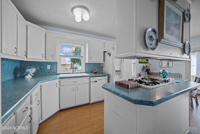 kitchen with white appliances, dark countertops, a sink, and white cabinetry