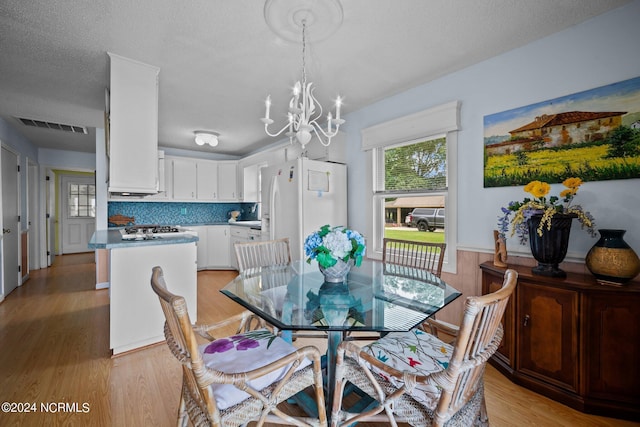 dining space featuring a wainscoted wall, visible vents, a textured ceiling, a chandelier, and light wood-type flooring