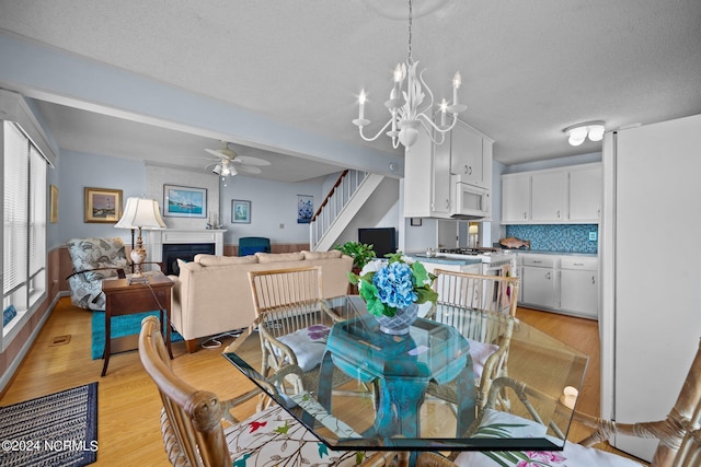 dining space featuring a textured ceiling, ceiling fan with notable chandelier, a fireplace, stairway, and light wood finished floors