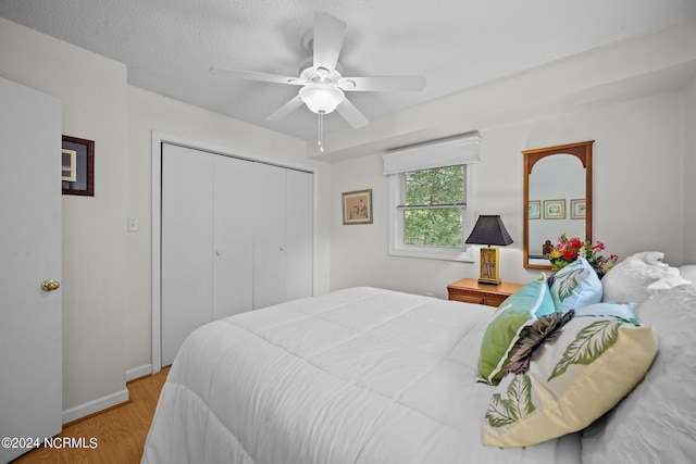 bedroom with a textured ceiling, wood finished floors, a ceiling fan, baseboards, and a closet