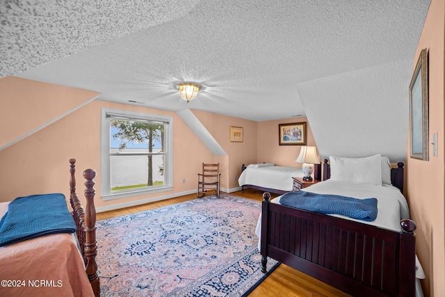 bedroom featuring lofted ceiling, a textured ceiling, baseboards, and wood finished floors