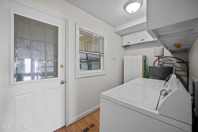 clothes washing area featuring visible vents, light wood-style flooring, a textured ceiling, washer and dryer, and laundry area