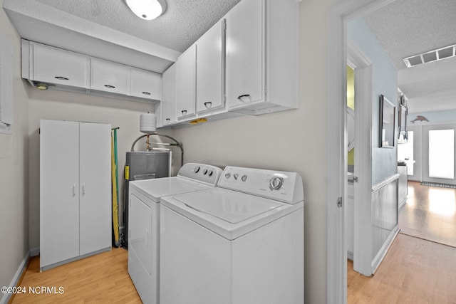 washroom with a textured ceiling, washing machine and dryer, visible vents, light wood-style floors, and cabinet space