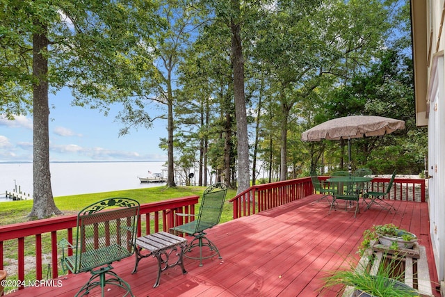 wooden deck with outdoor dining area, a water view, and a yard