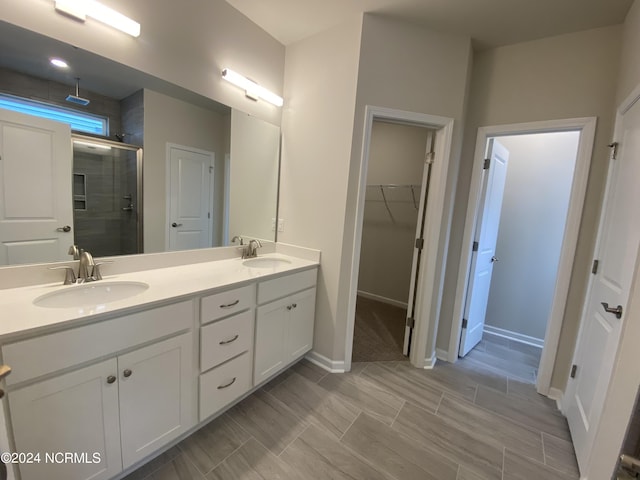 full bathroom featuring double vanity, a stall shower, a spacious closet, and a sink