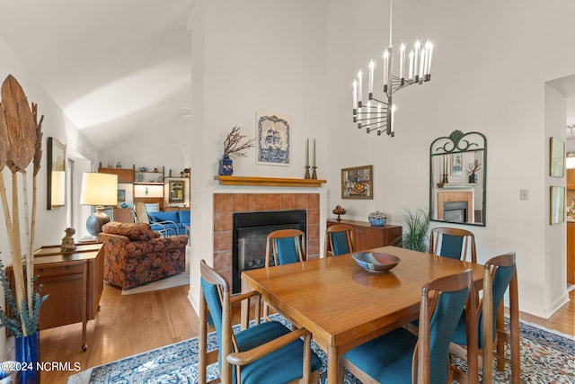 dining space with high vaulted ceiling, a chandelier, a tile fireplace, and hardwood / wood-style floors