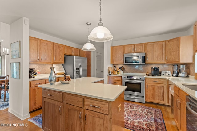 kitchen featuring a kitchen island, decorative light fixtures, backsplash, appliances with stainless steel finishes, and light hardwood / wood-style floors