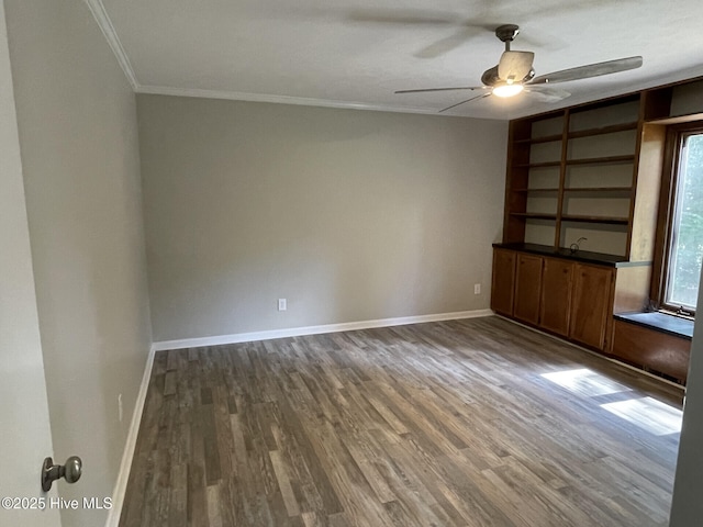 empty room featuring a ceiling fan, crown molding, baseboards, and wood finished floors