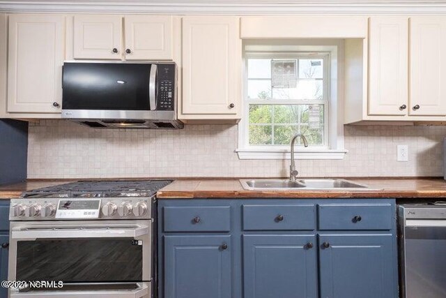 kitchen featuring blue cabinetry, stainless steel appliances, white cabinetry, and wood counters