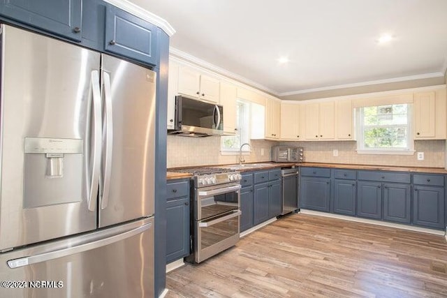 kitchen with blue cabinetry, backsplash, appliances with stainless steel finishes, ornamental molding, and a sink