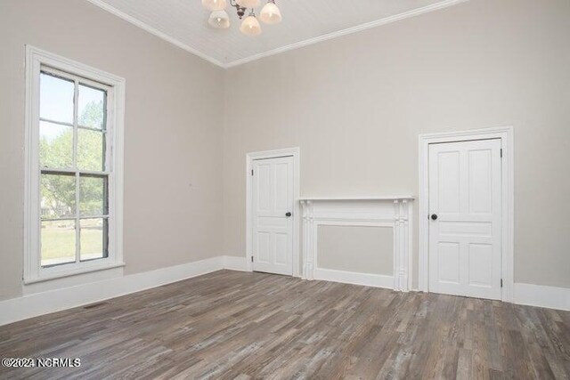 empty room with crown molding, dark hardwood / wood-style flooring, a notable chandelier, and a healthy amount of sunlight