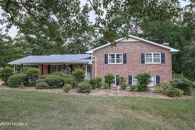 tri-level home featuring a chimney, a front lawn, and brick siding