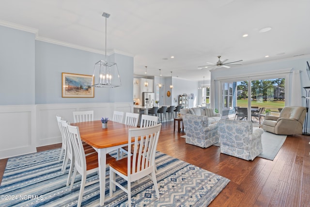 dining space with dark wood-style floors, a wainscoted wall, recessed lighting, ornamental molding, and ceiling fan with notable chandelier