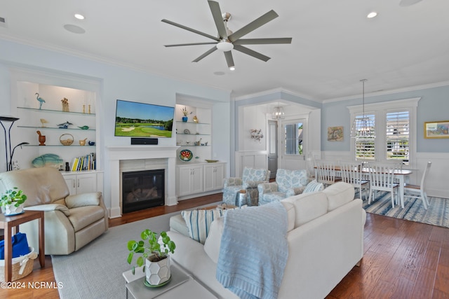 living room featuring built in features, wood-type flooring, ornamental molding, a glass covered fireplace, and wainscoting