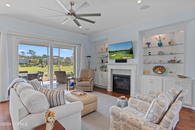 living room featuring built in shelves, recessed lighting, wood finished floors, a glass covered fireplace, and crown molding