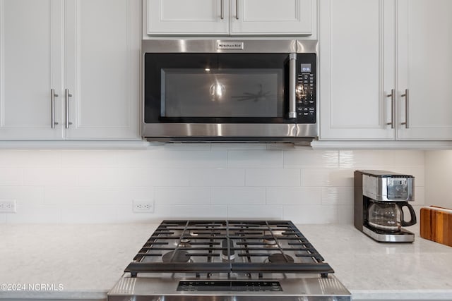 room details with light stone countertops, appliances with stainless steel finishes, white cabinets, and backsplash