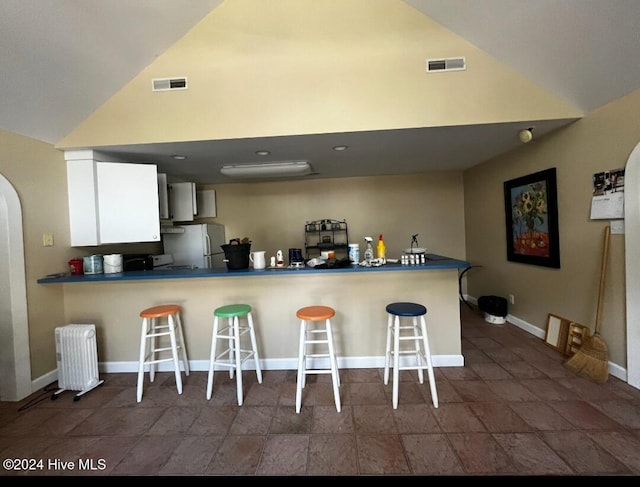 kitchen with a breakfast bar, visible vents, vaulted ceiling, freestanding refrigerator, and radiator heating unit