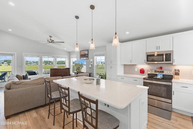 kitchen featuring open floor plan, stainless steel appliances, light wood finished floors, and vaulted ceiling