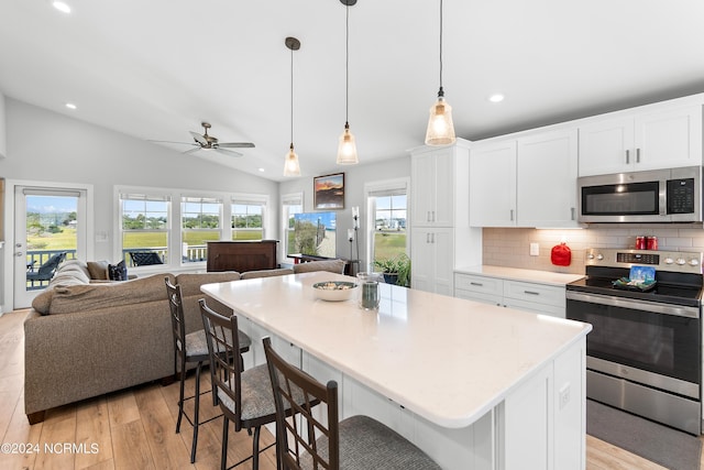 kitchen with white cabinets, open floor plan, vaulted ceiling, stainless steel appliances, and light wood-type flooring