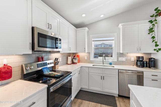 kitchen featuring light wood finished floors, stainless steel appliances, tasteful backsplash, white cabinets, and a sink