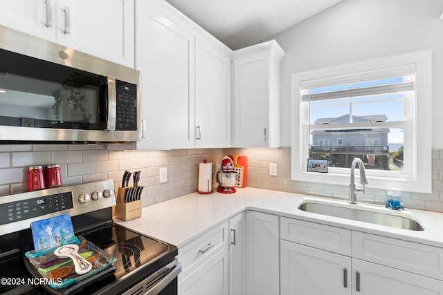 kitchen featuring white cabinets, a sink, stainless steel appliances, light countertops, and backsplash