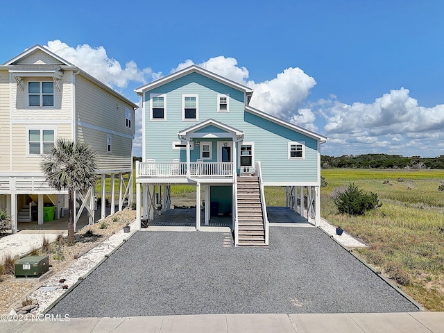 view of front of home with a carport, gravel driveway, a porch, and stairway