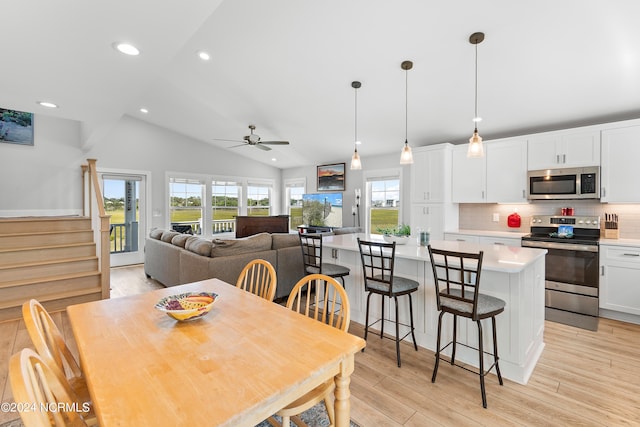 dining space featuring stairway, light wood-type flooring, a healthy amount of sunlight, and lofted ceiling