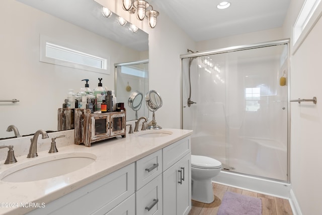 bathroom featuring double vanity, a shower stall, a sink, and wood finished floors