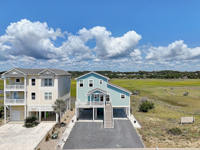 coastal inspired home with driveway, covered porch, stairs, and a carport