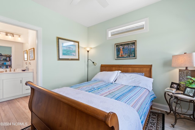 bedroom featuring baseboards, light wood-style flooring, ceiling fan, ensuite bathroom, and a sink