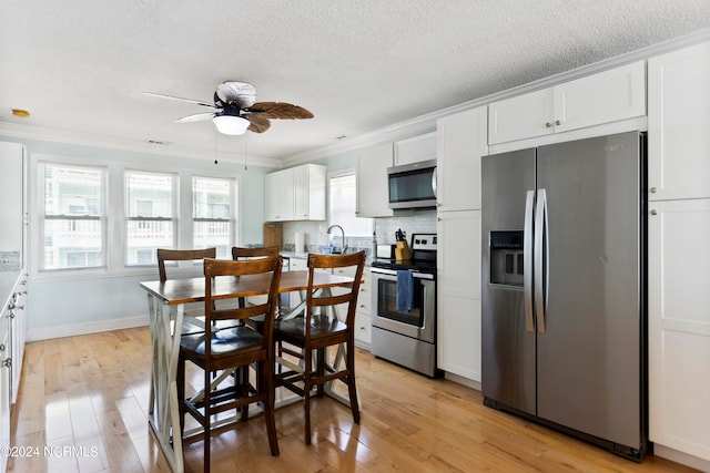 kitchen with ceiling fan, stainless steel appliances, white cabinetry, and light hardwood / wood-style flooring