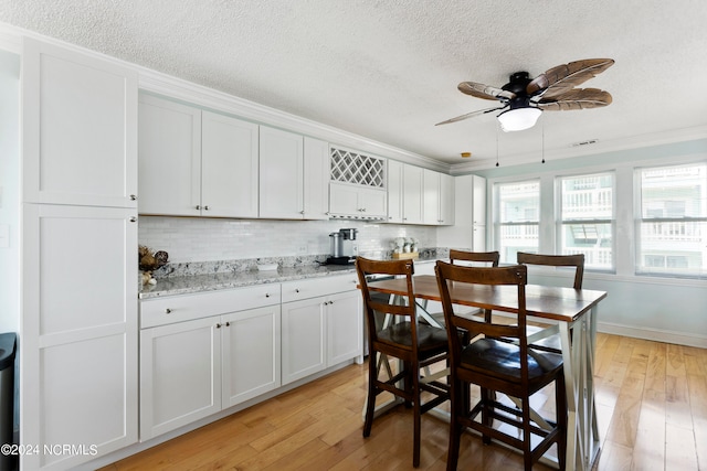 kitchen with white cabinets, light hardwood / wood-style floors, ceiling fan, decorative backsplash, and ornamental molding