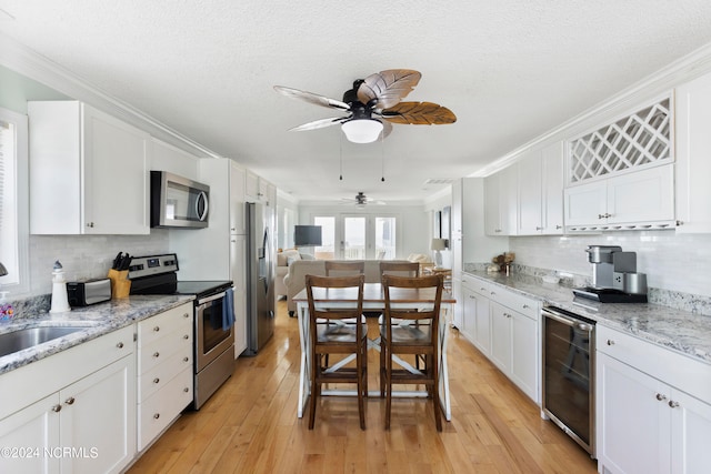 kitchen with beverage cooler, stainless steel appliances, ceiling fan, and light hardwood / wood-style floors