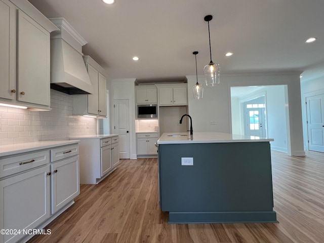 kitchen featuring light hardwood / wood-style floors, ornamental molding, sink, and an island with sink