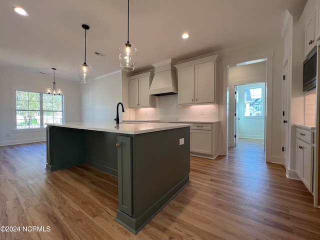 kitchen featuring plenty of natural light, premium range hood, and an island with sink