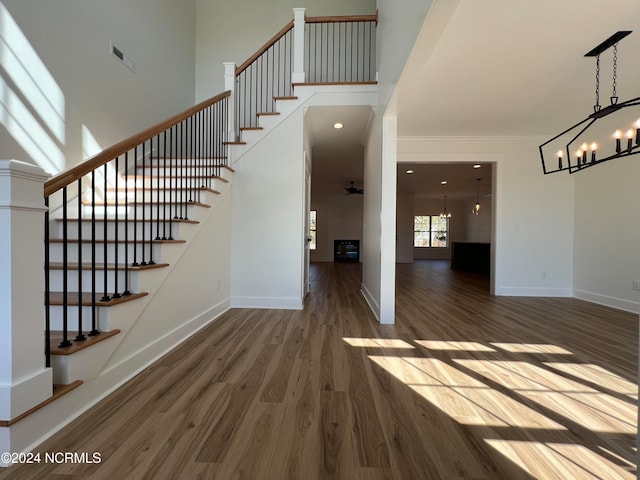 stairs featuring crown molding, hardwood / wood-style floors, ceiling fan with notable chandelier, and a high ceiling