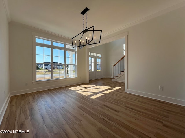 unfurnished dining area with french doors, crown molding, a notable chandelier, and wood-type flooring