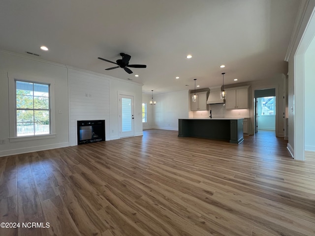 unfurnished living room featuring wood-type flooring, a large fireplace, ornamental molding, sink, and ceiling fan