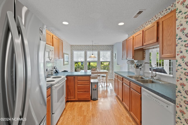 kitchen with dark countertops, white appliances, a sink, and wallpapered walls