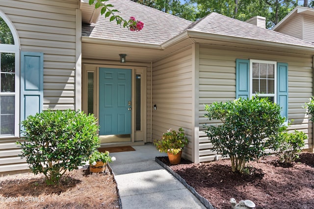 view of exterior entry featuring roof with shingles