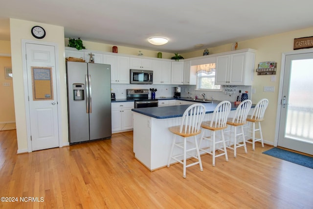 kitchen with light hardwood / wood-style flooring, appliances with stainless steel finishes, white cabinetry, kitchen peninsula, and a kitchen breakfast bar