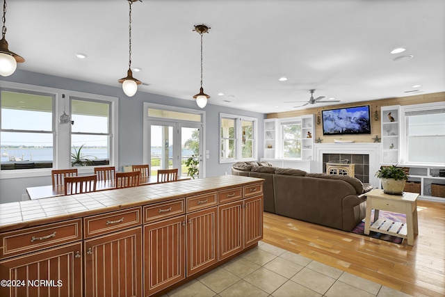 kitchen with ceiling fan, a tile fireplace, pendant lighting, tile counters, and light tile patterned floors