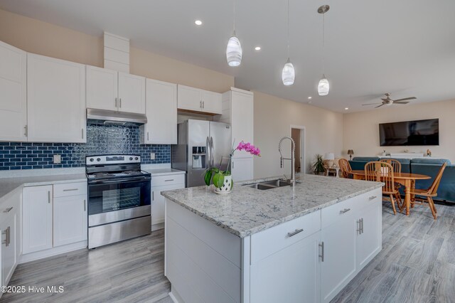 kitchen with an island with sink, stainless steel appliances, white cabinets, light stone counters, and sink